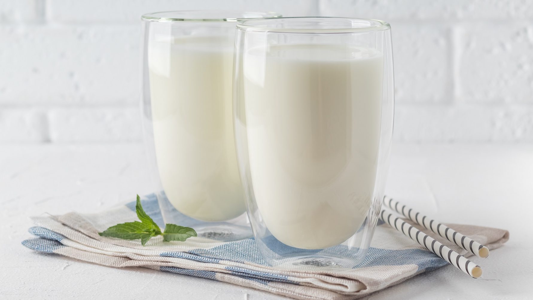 Vor einer weißen Wand stehen zwei Gläser, die mit dem türkischen Nationalgetränk Ayran gefüllt sind. Die Gläser stehen auf einem Handtuch.