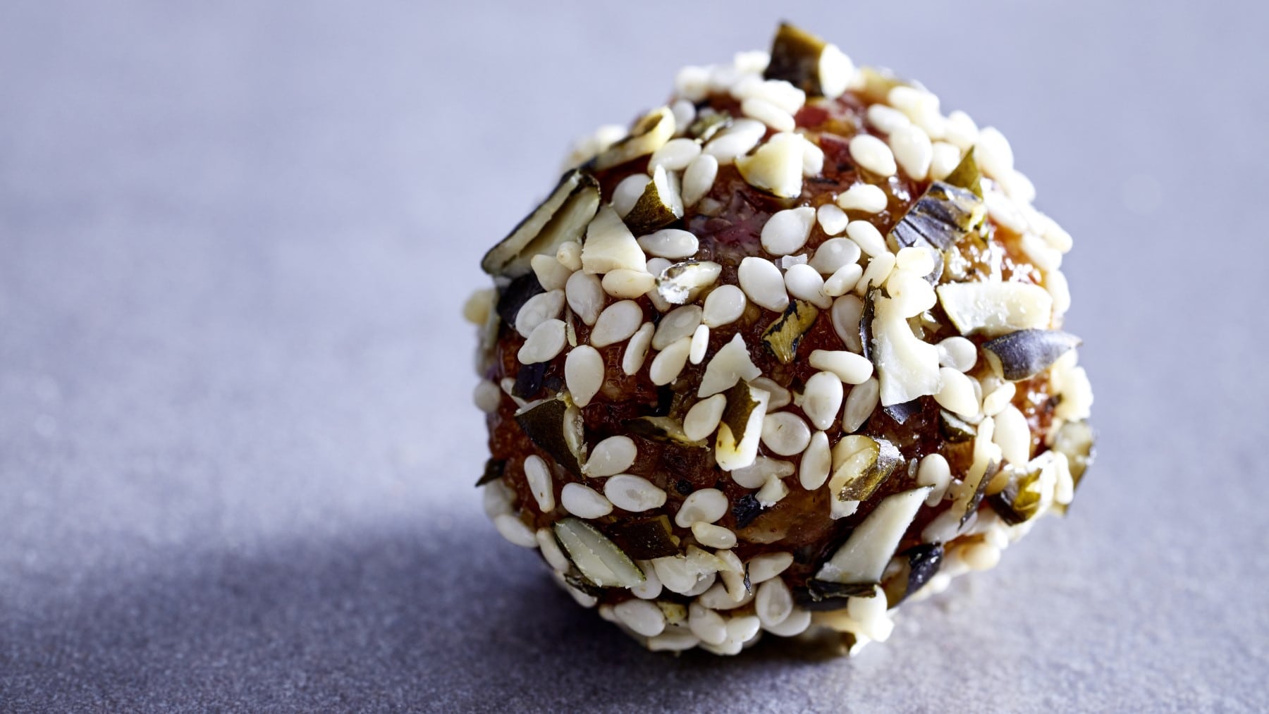 Ein Aprikosen-Sesam-Ball auf einem grauen Hintergrund.